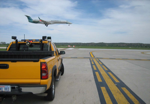 Car waiting on runway with plane landing